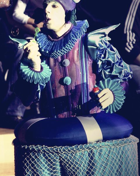 Payaso del Circo Acuático, con gorro de caracola y gorguera azul, sentado sobre un flotador.