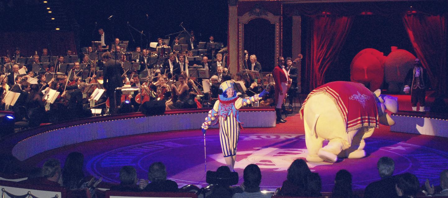 Pista del circo Roncalli con una orquesta sinfónica al fondo, un payaso y un hipopótamo animatrónico.